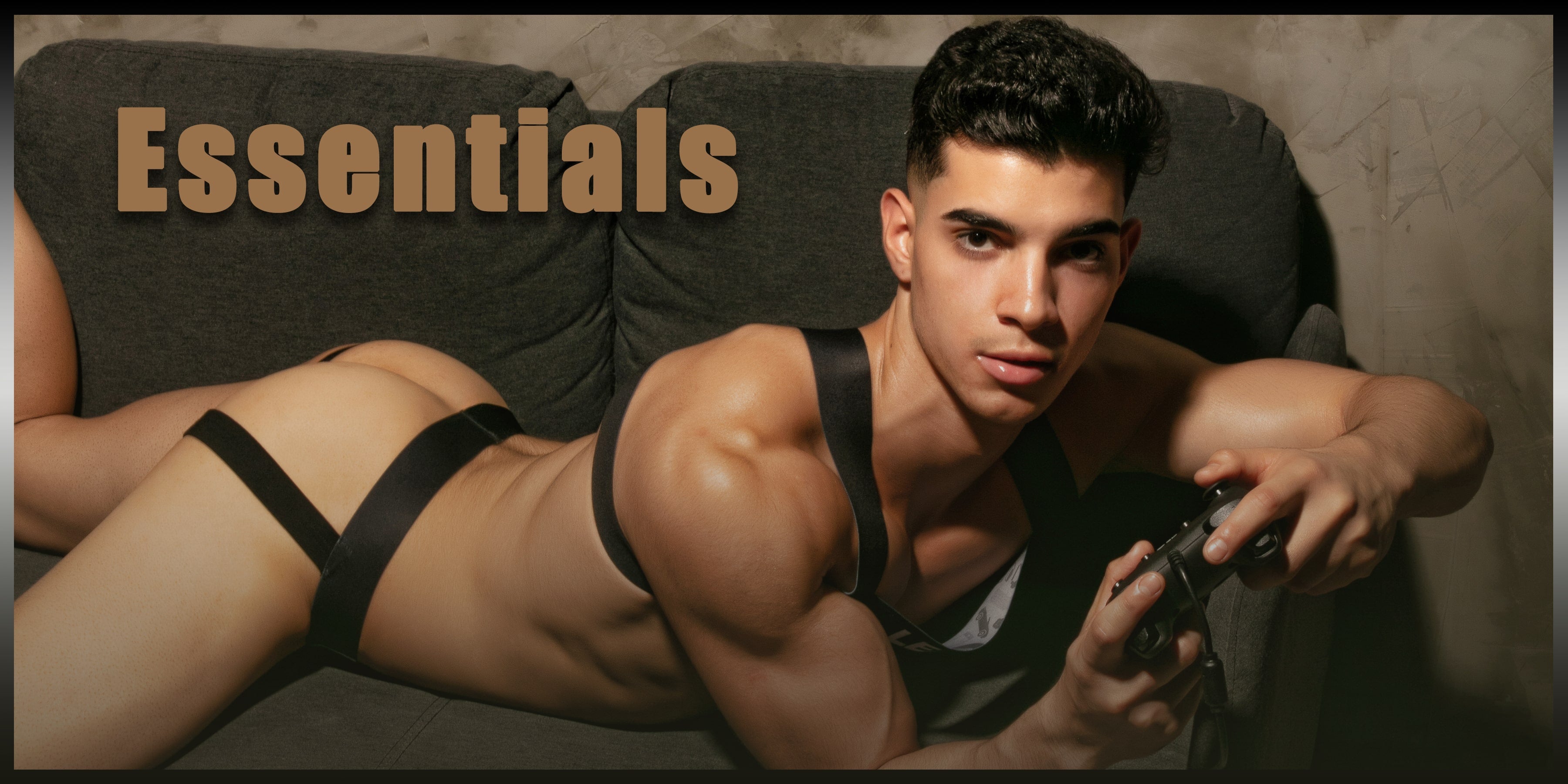 Hot LEADER model Leo red wearing Essentials Collection Harness and Jockstrap whilst lying on the sofa playing games